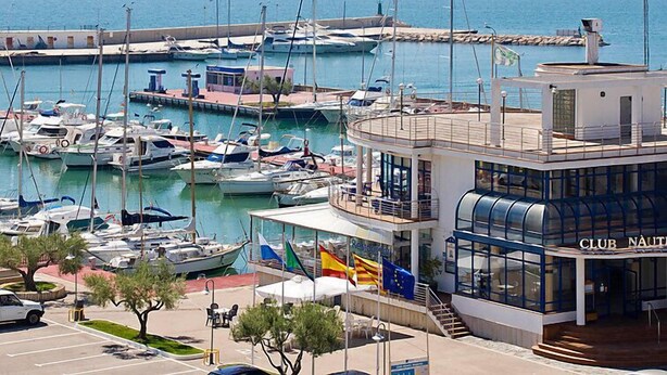 A marina with multiple boats docked, a restaurant named "Club Nautica," and a clear view of the sea. - Edificio Nautic by Interhome (L'Ampolla)
