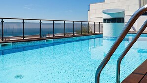 A clear blue pool with a view of the ocean, a modern building with a white facade, and a metal pool ladder. - Edificio Nautic by Interhome (L'Ampolla)