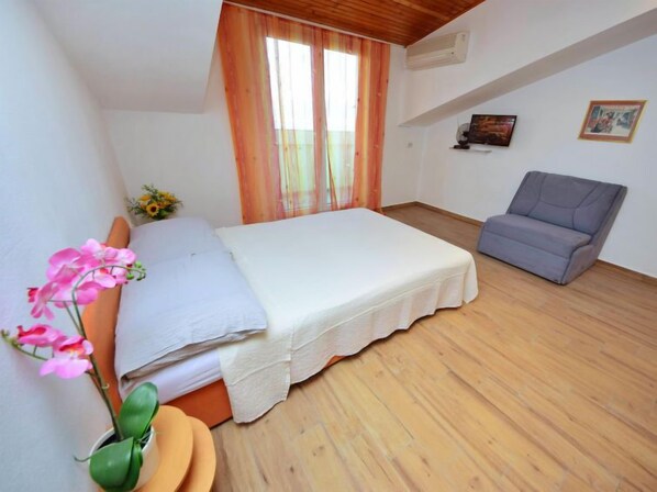 A bedroom with a bed, a chair, a potted plant, and a window with curtains. - Apartment Šarić by Interhome (Trogir/Arbanija)