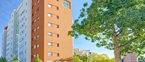 A multi-story building with balconies, a stone wall, and a tree in the foreground.