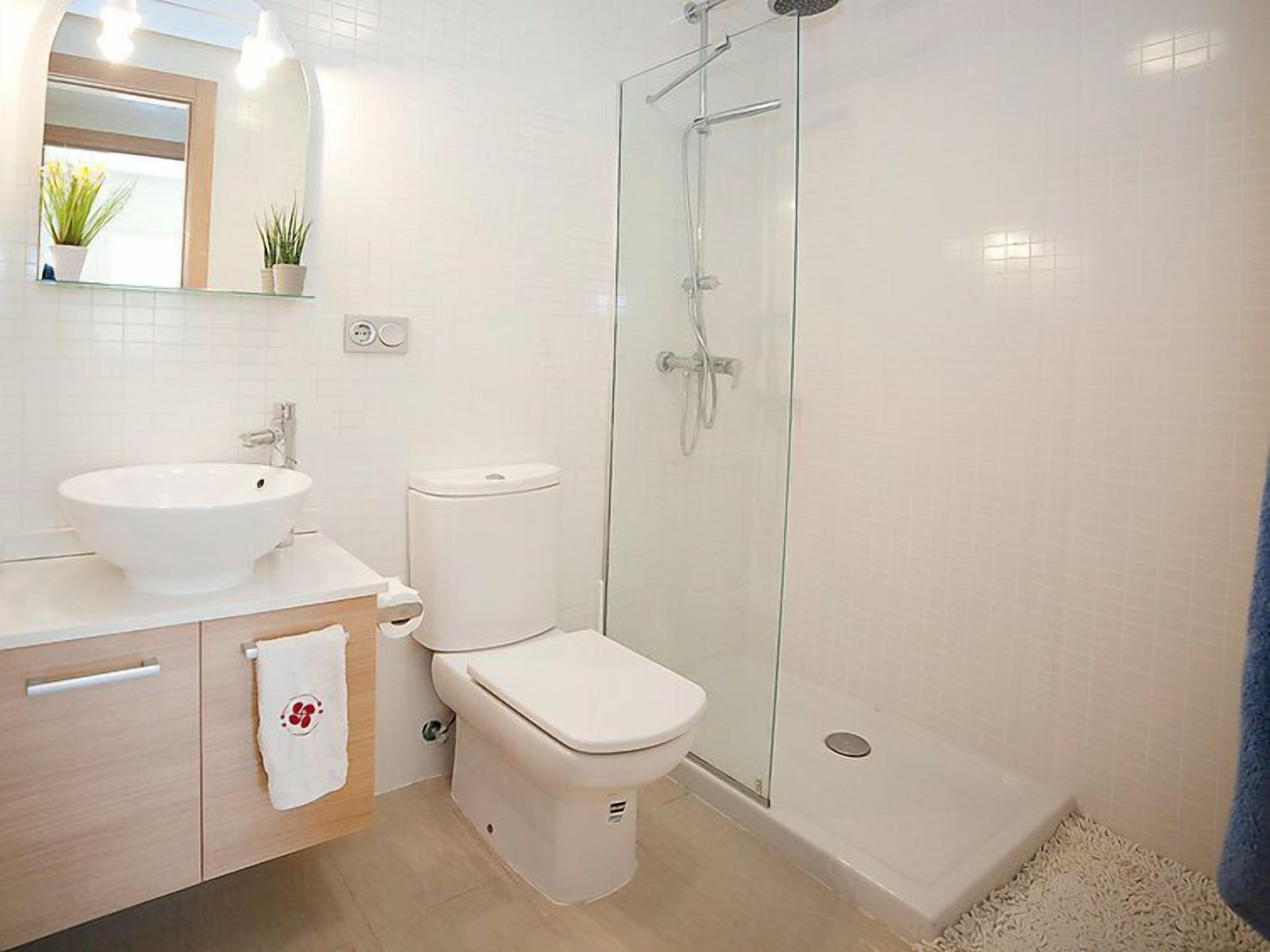 Une salle de bain moderne avec un lavabo blanc, des toilettes et une douche à parois de verre.