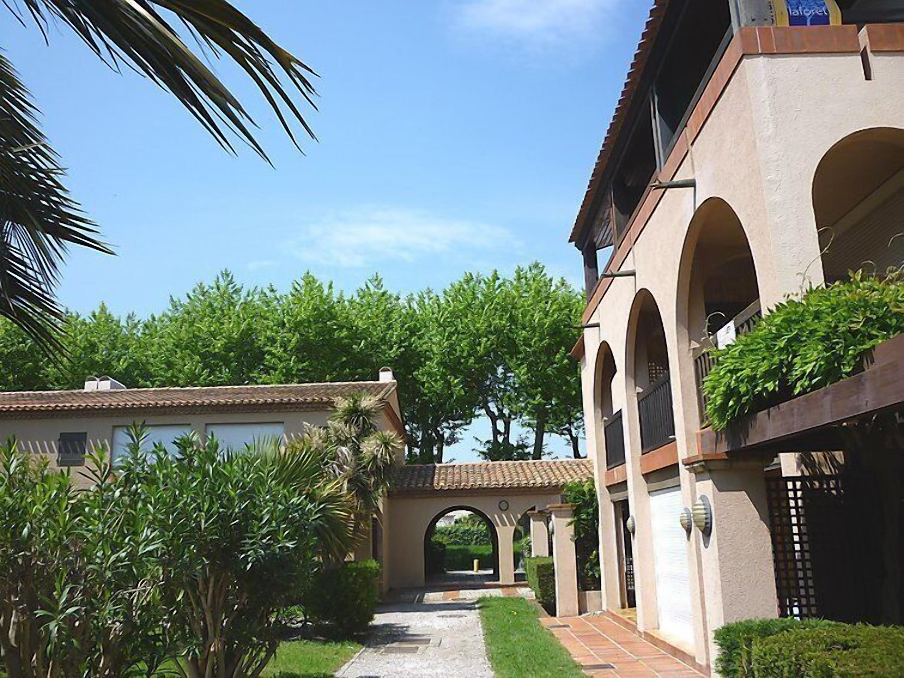 A building with a covered walkway, arches, and lush greenery.