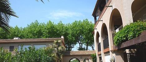 A building with a covered walkway, arches, and lush greenery.