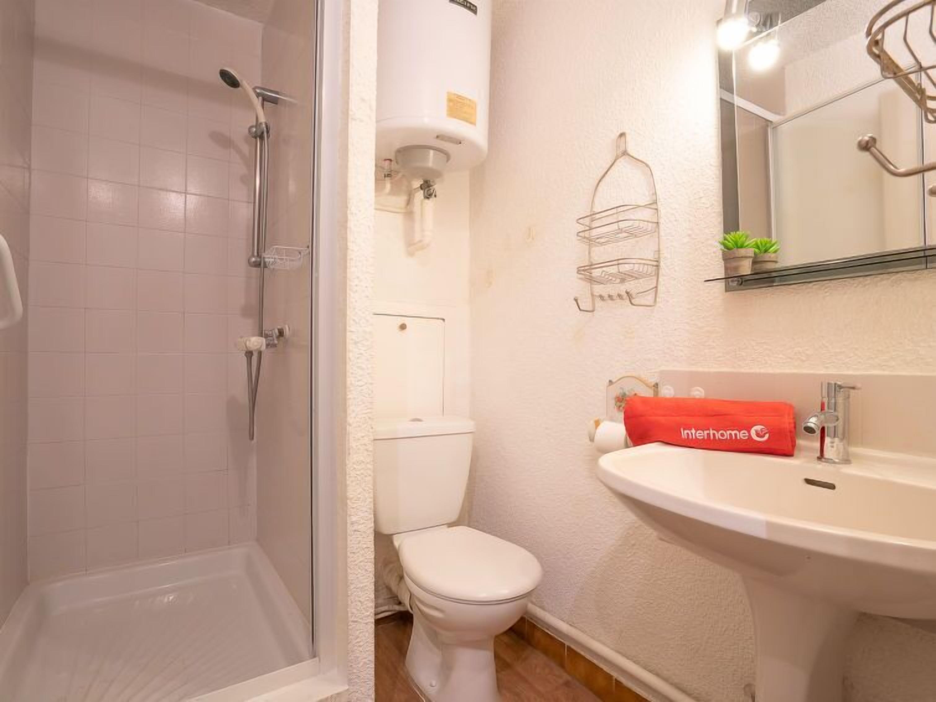 A bathroom with a glass-enclosed shower, a toilet, and a sink with a towel.