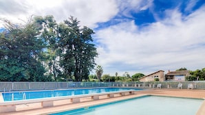 Una piscina rectangular con superficie de agua azul cristalina, rodeada por un muro de piedra bajo y una cerca metálica.