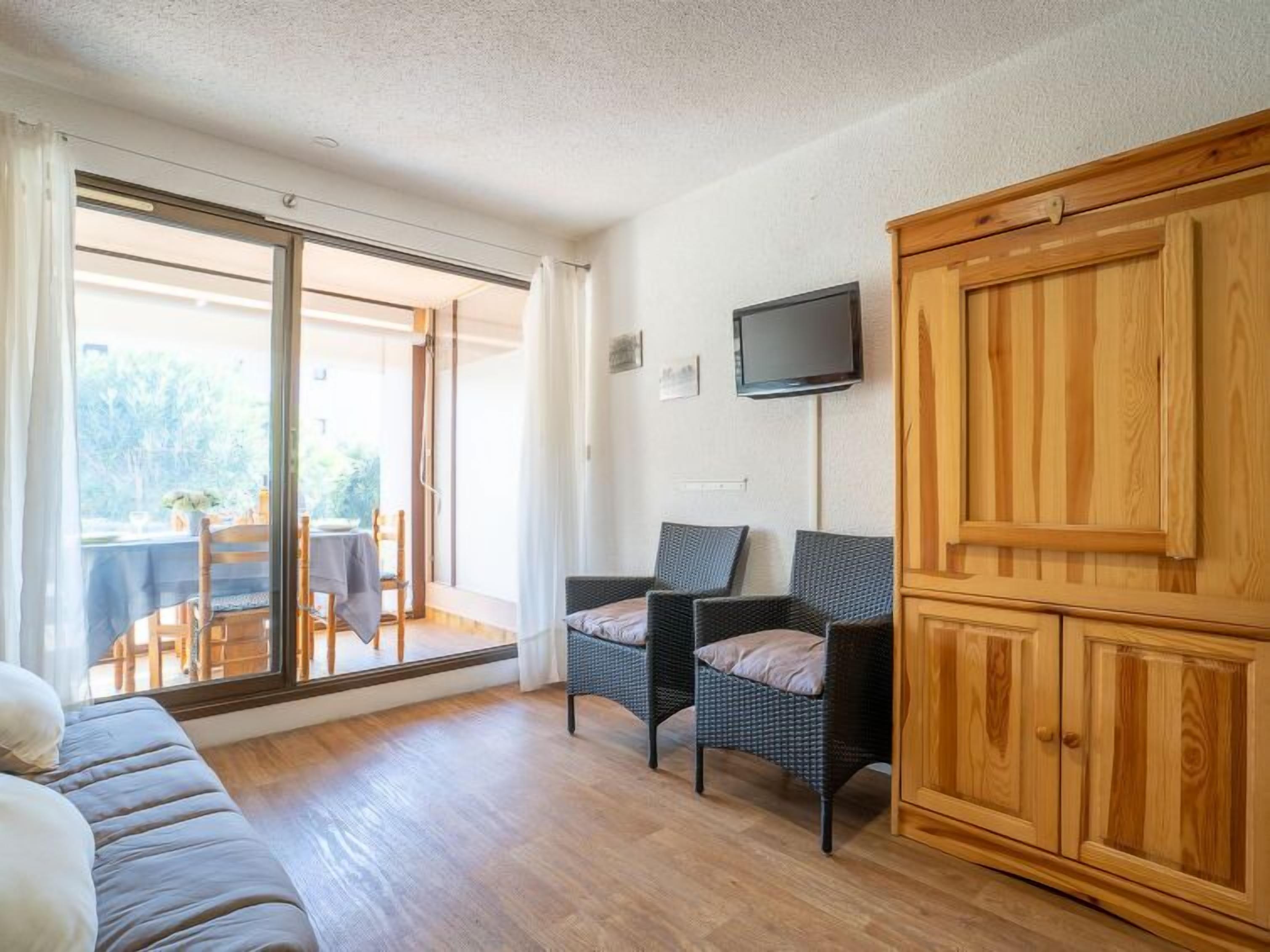 A room with a sofa, two wicker chairs, a TV on the wall, and a wooden cabinet.