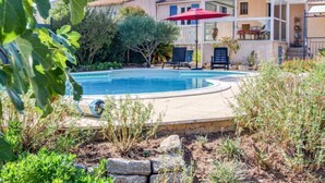 A swimming pool surrounded by a garden with various plants and a covered patio area with outdoor furniture. - Les Hauts de Palayson by Interhome (Le Muy)