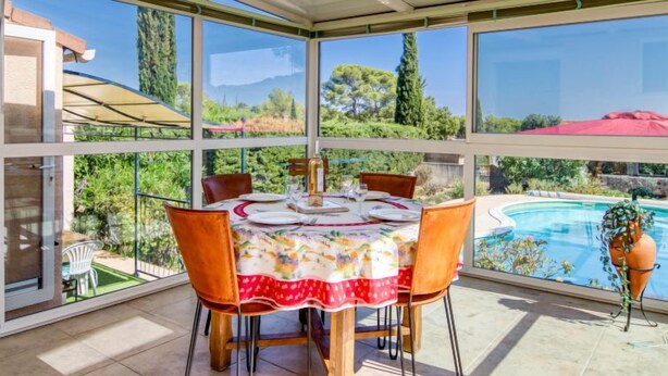 A sunlit patio with a table set for dining, overlooking a swimming pool and lush greenery. - Les Hauts de Palayson by Interhome (Le Muy)