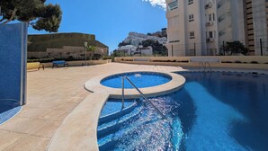 Une piscine baignée de lumière, un mur de pierre et un bâtiment en arrière-plan.