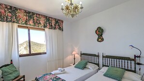 Une chambre d’hôtel avec deux lits, une fenêtre avec des rideaux, un lustre, une horloge murale et une petite table avec une lampe.