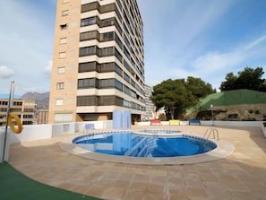 A rooftop swimming pool with a view of a tall building and a hilly landscape.