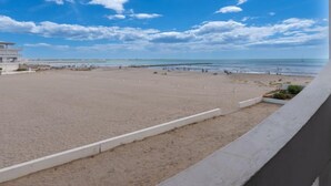 Une plage avec un bâtiment en arrière-plan, un ciel dégagé et une rive sablonneuse.