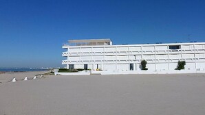 Un bâtiment moderne de couleur blanche, doté de plusieurs étages, situé près d’une plage.