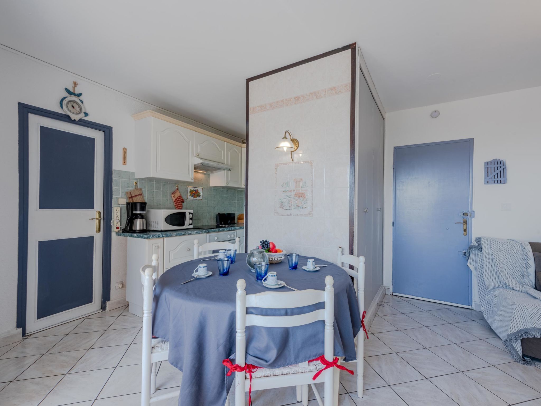 A dining area with a table set for two, a kitchen in the background, and a blue door.