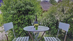 A round table with two chairs, a bottle, and a glass, set against a backdrop of lush greenery and a mountain.