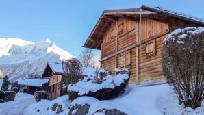 A wooden chalet with a sloped roof, surrounded by snow-covered rocks and mountains in the background.