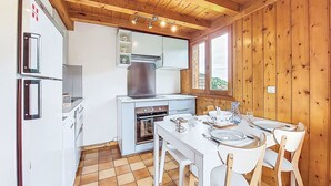 A kitchen with a stove, oven, and white cabinets. There is a dining table with chairs and a window with a view of the outdoors.