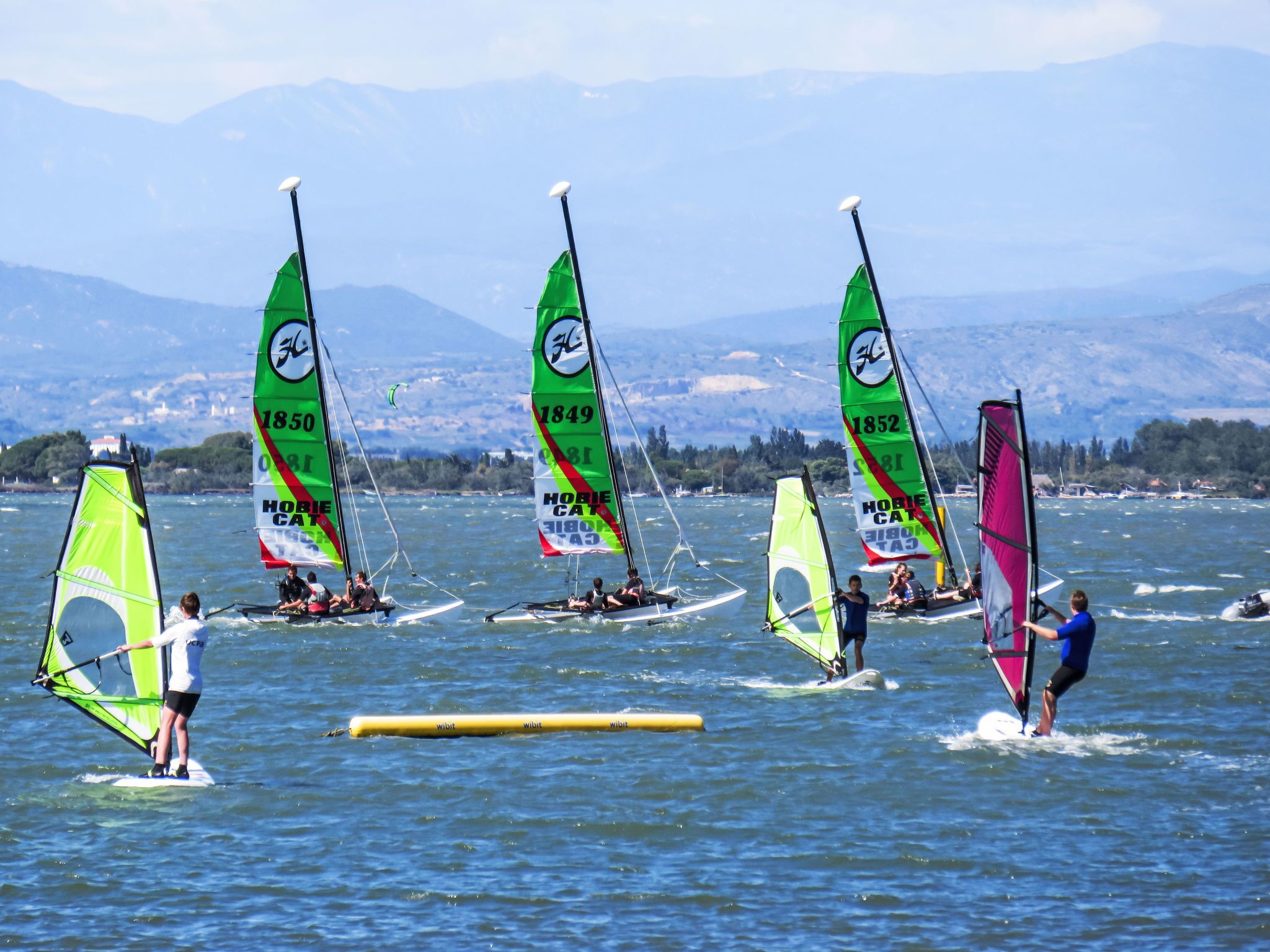 A group of windsurfing boats on a lake with mountains in the background.