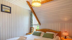 Une chambre avec un plafond en bois, un lit recouvert de draps blancs, des oreillers verts et une table de chevet avec une lampe.