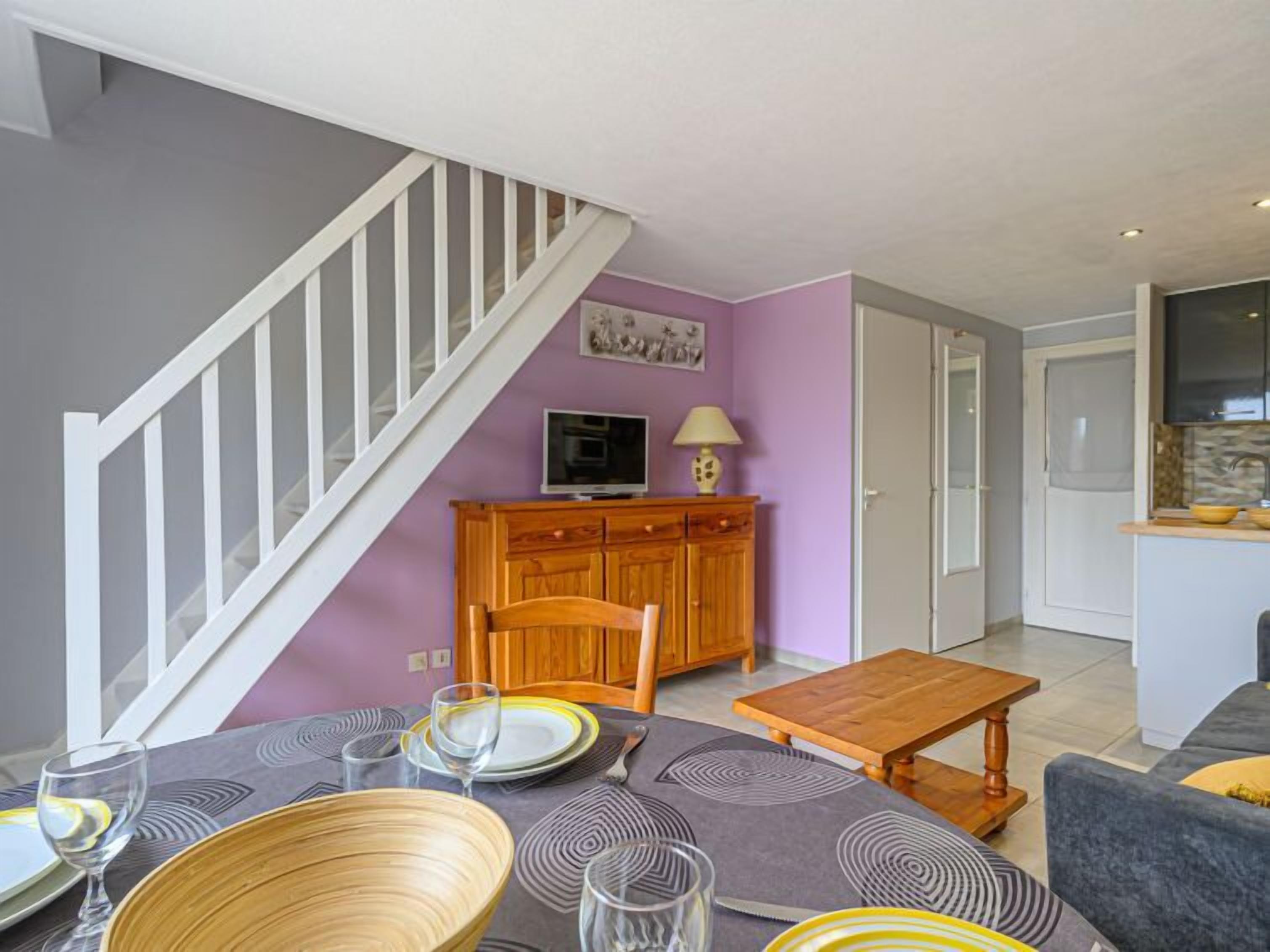 A dining area with a table set for four, a wooden cabinet, and a staircase.