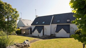 Une rangée de maisons aux toits inclinés et aux petites fenêtres, entourées d’une pelouse verdoyante et d’un mur de pierre.