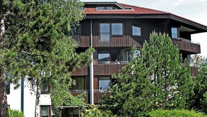 Un edificio de varios pisos con balcones, rodeado de abundante vegetación.