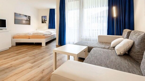 Una habitación de hotel moderna con una cama, un sofá, una mesita y un televisor.