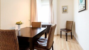 Un comedor con una mesa de madera oscura, sillas de mimbre, un jarrón con flores y un cuadro en la pared.