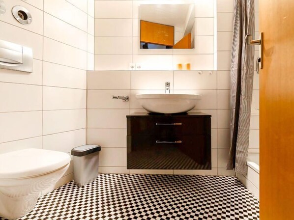 A bathroom with a white toilet, a black and white checkered floor, a white sink on a dark cabinet, and a mirror above the sink.