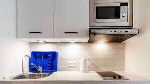 Una cocina moderna con armarios blancos, un lavamanos de acero inoxidable, un microondas y una tetera.