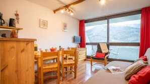 Um quarto aconchegante com uma mesa de jantar de madeira, cadeiras, um sofá e uma grande janela com vista para montanhas.