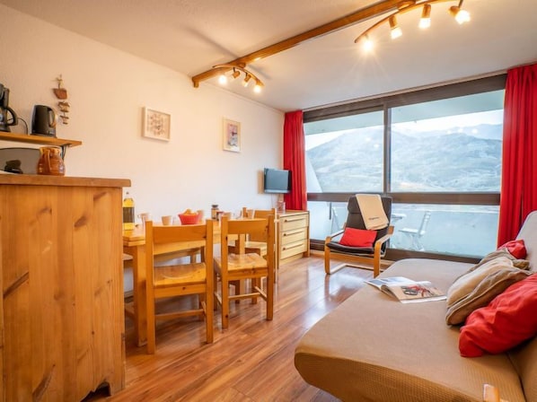 Une pièce chaleureuse avec une table à manger en bois, des chaises, un canapé et une grande fenêtre donnant sur les montagnes.