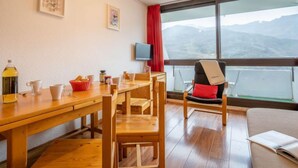 Um quarto aconchegante com uma mesa de jantar de madeira, cadeiras, um sofá, uma TV e uma grande janela com vista para as montanhas.