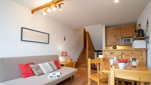 Uma sala de estar aconchegante com um sofá, uma mesa de jantar de madeira e uma área de cozinha com armários de madeira e um micro-ondas.
