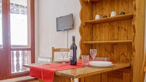 A wooden dining table with a red tablecloth, a bottle of wine, and two glasses. A television is mounted on the wall above the table. - Rond Point des Pistes (Val Claret) by Interhome (Tignes)