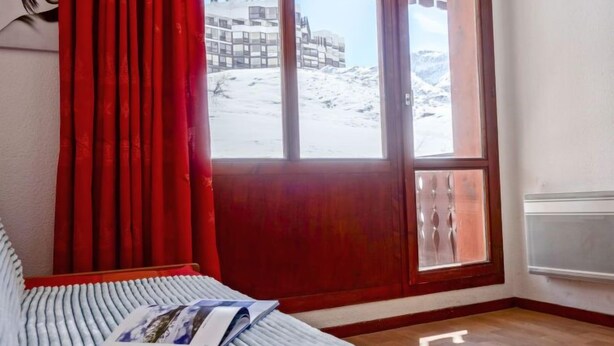A room with a bed, a window with a view of a snowy landscape, and a red curtain. - Rond Point des Pistes (Val Claret) by Interhome (Tignes)
