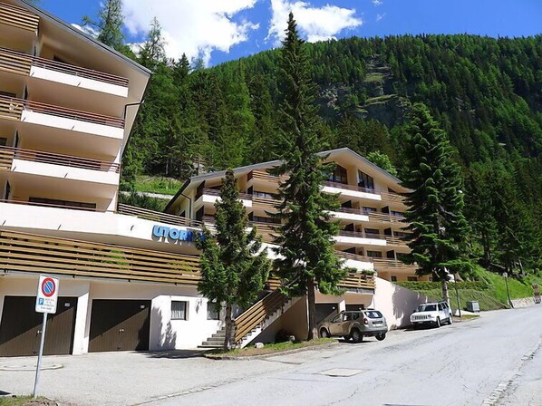 Een hotel met meerdere verdiepingen, balkons, een parkeerplaats en een bergachtig achtergrondlandschap.