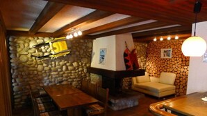 Un intérieur chaleureux avec un mur en pierre, des poutres apparentes en bois au plafond, une cheminée et un canapé.
