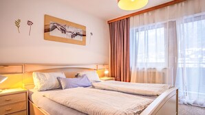 A double bed with a headboard, bedside tables with lamps, a wall-mounted artwork, and sheer curtains. - Bichleregg by Interhome (Ötz)
