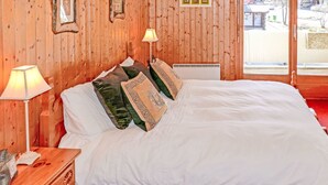 A wooden-paneled room with a bed, two bedside lamps, and framed pictures on the wall. - Grand Place 5 by Interhome (Nendaz)