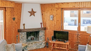 A cozy living room with a stone fireplace, wooden walls, a television, and a comfortable seating area. - Grand Place 5 by Interhome (Nendaz)
