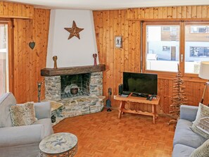 Ein gemütliches Wohnzimmer mit Kamin aus Stein, Holzwänden, einem Fernseher und einer bequemen Sitzecke.