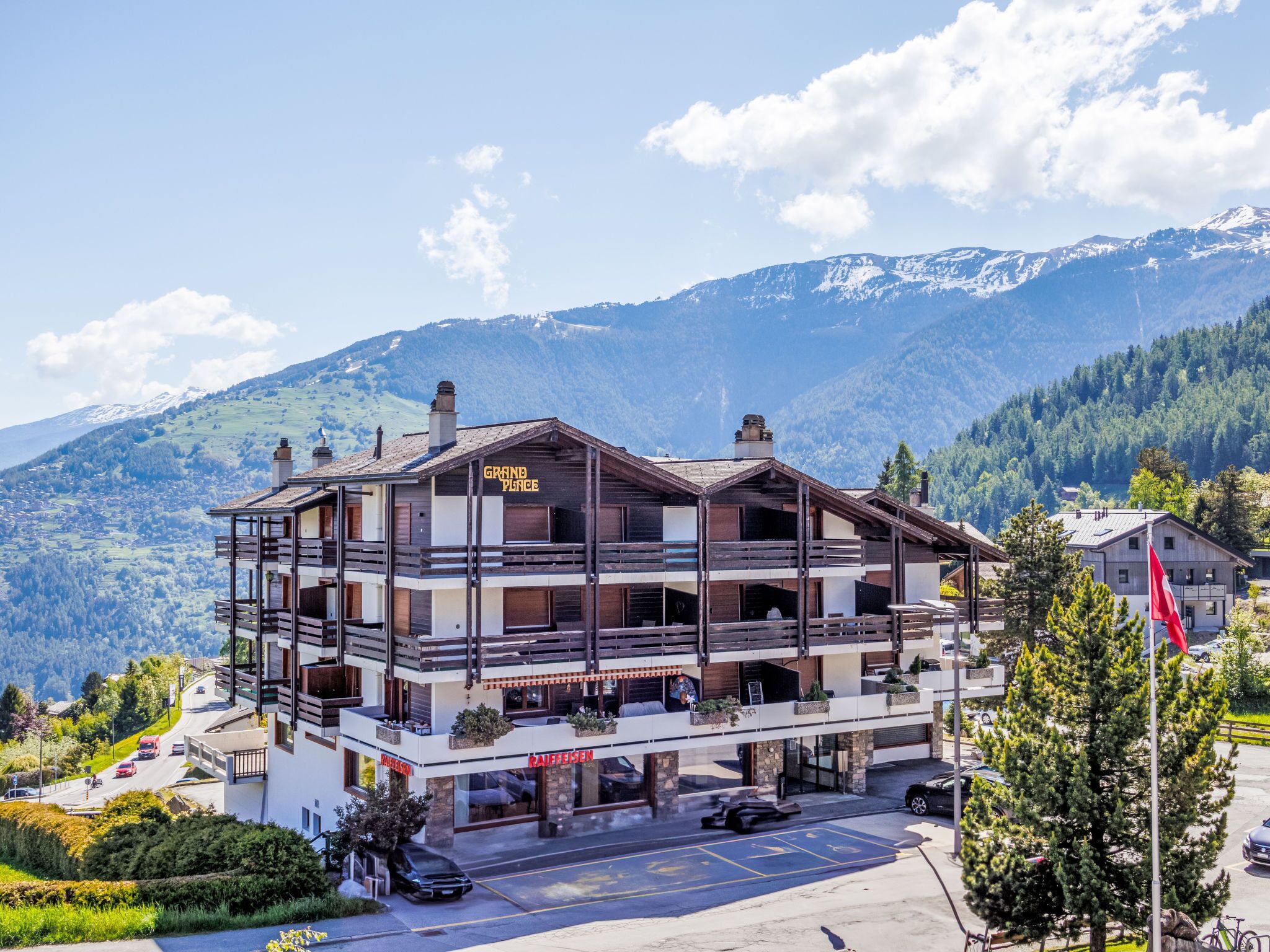 A multi-story hotel with a mountain backdrop, featuring a restaurant and a ski lift visible in the parking area.