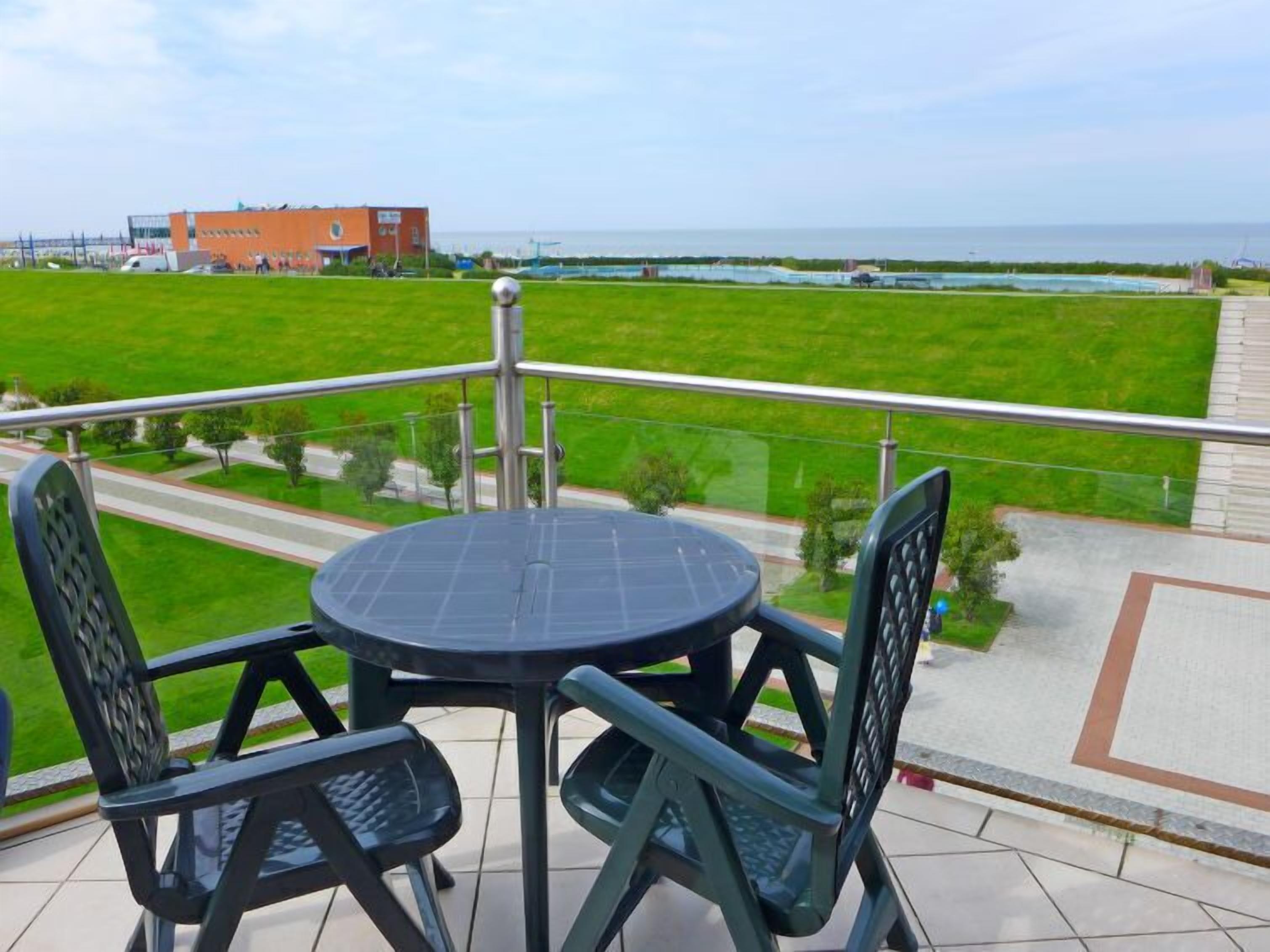 Ein Balkon mit Tisch und Stühlen, mit Blick auf eine Wiese und ein Gewässer.