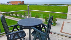 A balcony with a table and chairs, overlooking a grassy area and a body of water. - Meerblick by Interhome (Norddeich)