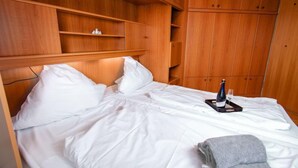 A bed with white linens, a bedside table with a bottle and glass, and wooden wardrobe with multiple compartments. - Meerblick by Interhome (Norddeich)