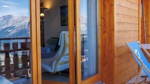 A wooden cabin with a glass door leading to a room with a bed and a chair. - Grand Panorama A11 by Interhome (Nendaz)