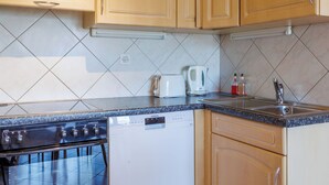A kitchen with wooden cabinets, a dishwasher, a stove, and a tiled backsplash. - Grand Panorama A11 by Interhome (Nendaz)
