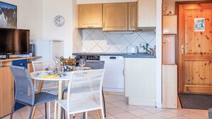 A compact kitchen with wooden cabinets, a built-in oven, and a dining area with two chairs and a table set for two. - Grand Panorama A11 by Interhome (Nendaz)