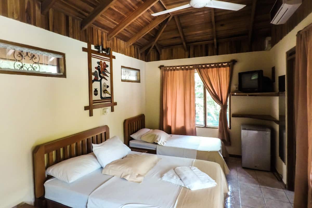 A room with two beds, a ceiling fan, a television, and a refrigerator.